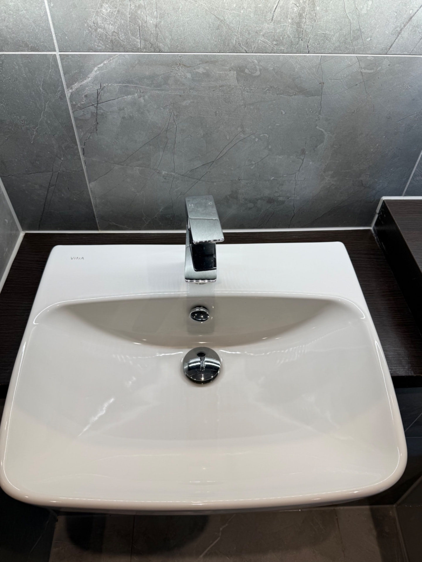 Wall-hung basin and chrome tap against grey tiling